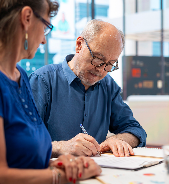 Two people discuss in a modern office, one taking notes while the other observes.